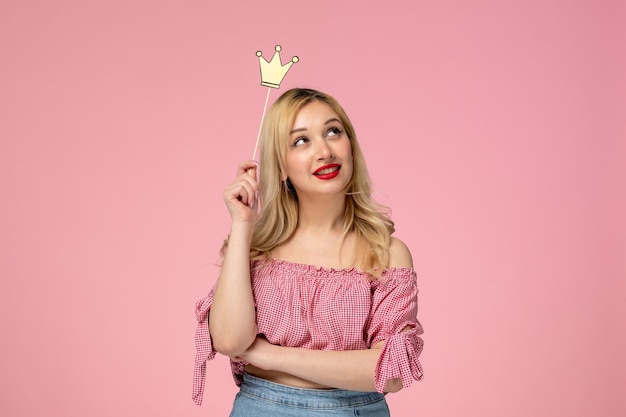 Foto grátis linda garota loira usando batom vermelho na blusa rosa pensando e segurando uma coroa