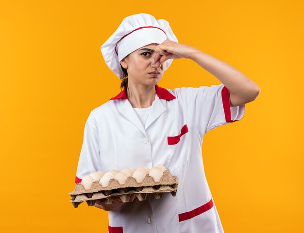 Foto grátis linda garota melindrosa com uniforme de chef segurando lote de ovos com o nariz fechado