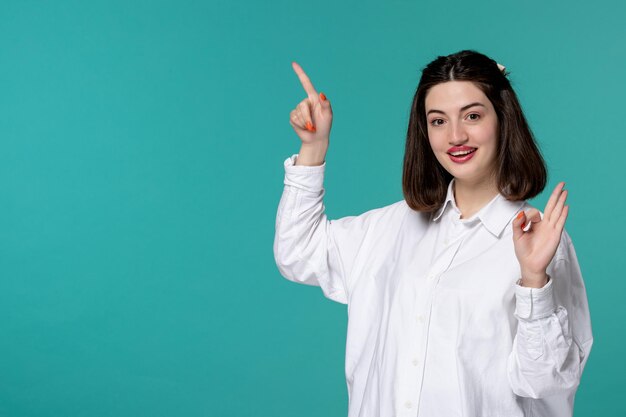 Linda garota morena jovem doce de camisa branca alegre apontando para cima