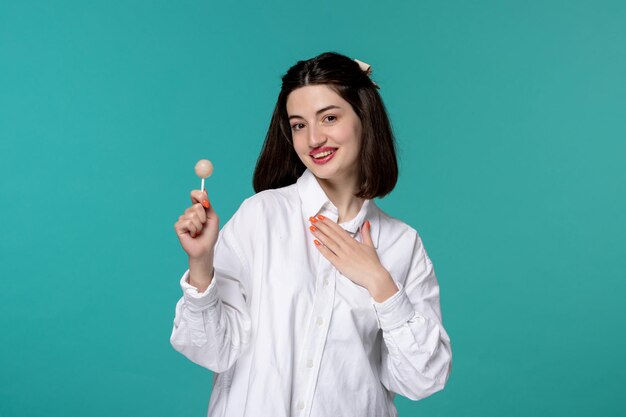 Linda garota morena muito adorável na camisa branca segurando o peito e um pirulito branco