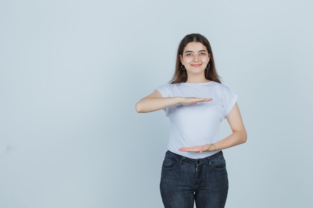 Foto grátis linda garota mostrando sinal de tamanho em camiseta, jeans e bonito, vista frontal.