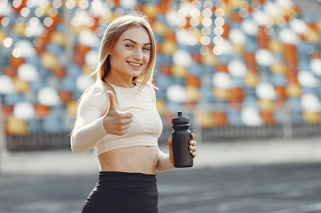 Linda garota no estádio. garota de esportes em um sportswear. mulher com garrafa de água.