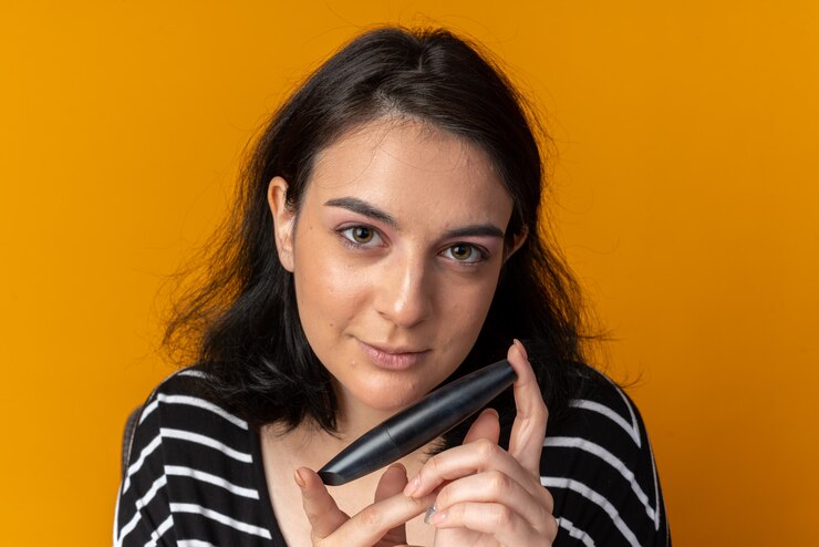 Foto grátis linda garota olhando impressionada segurando rímel isolado na parede laranja