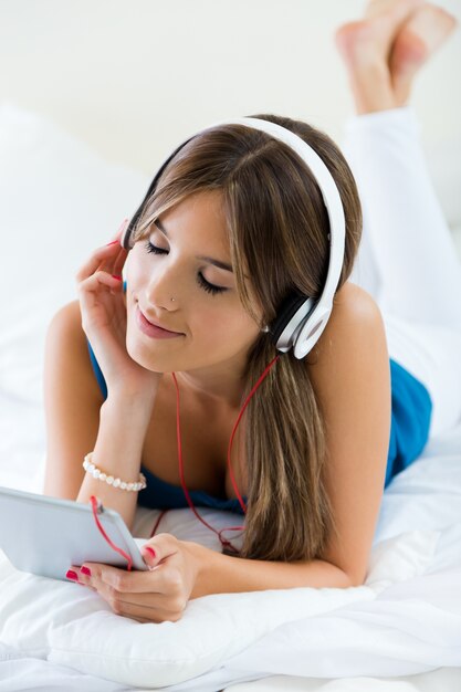 Linda garota ouvindo música com tablet no sofá em casa.