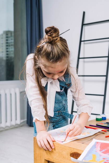 Linda garota pintando com aquarelle na folha de papel na mesa