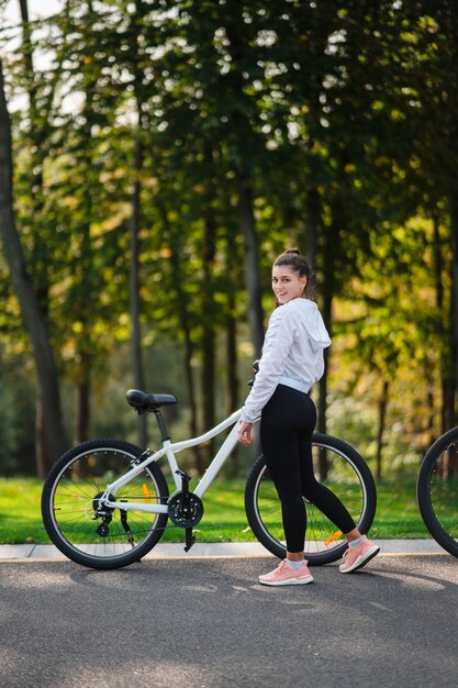 Linda garota posando em bicicleta branca. Caminhe na natureza. Estilo de vida saudável.