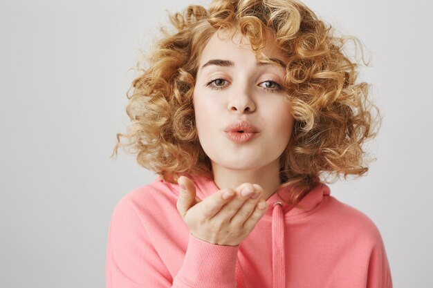 Linda garota romântica com cabelo encaracolado mandando beijo no ar