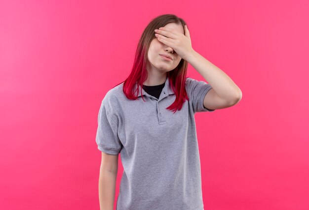 Linda garota satisfeita com uma camiseta cinza coberta com os olhos e a mão no fundo rosa isolado