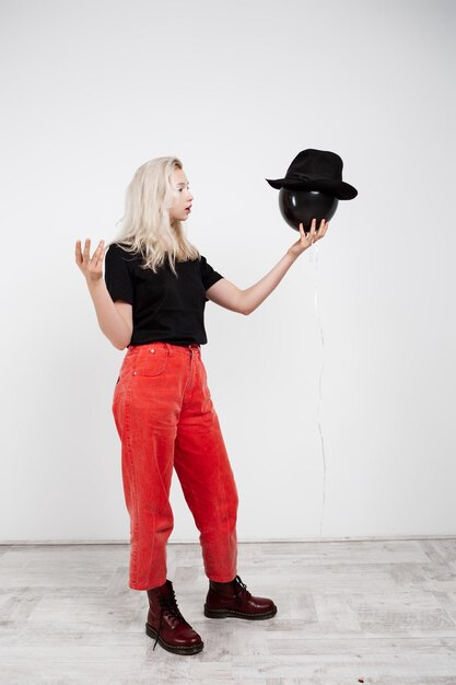 Linda garota segurando o balão no chapéu sobre parede branca