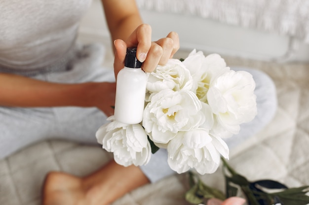 Linda garota segurando uma garrafa de creme e buquê de flores