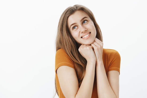 Linda garota sonhadora parecendo romântica, sorrindo e suspirando, olhando o canto superior esquerdo com admiração, sonhando acordada