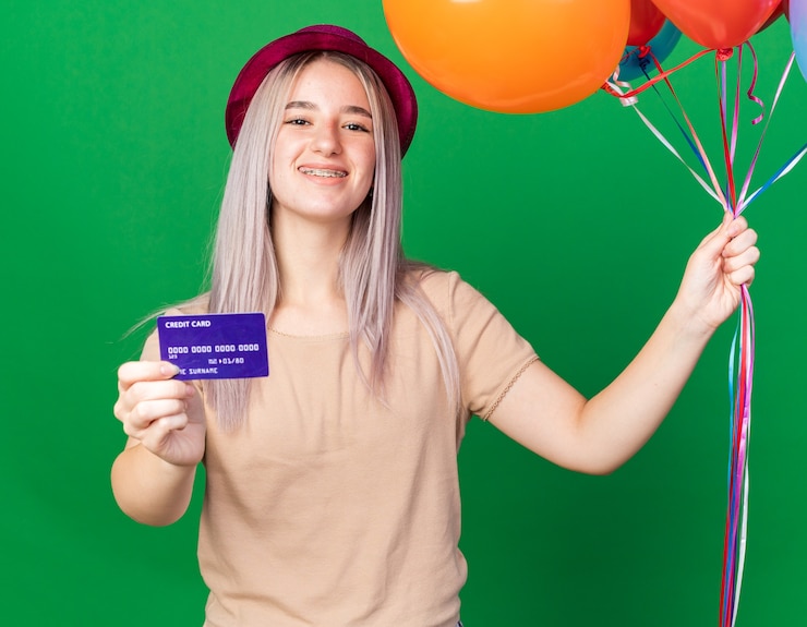 Foto grátis linda garota sorridente com chapéu de festa e suspensórios segurando balões com cartão de crédito