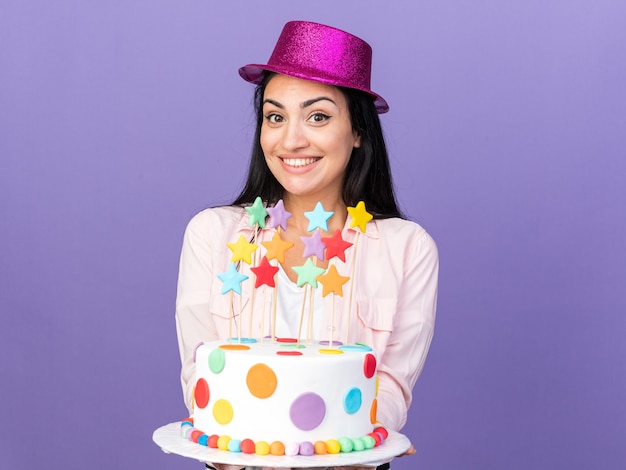 Linda garota sorridente com chapéu de festa segurando um bolo para a câmera