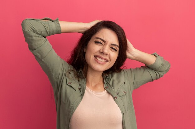 Linda garota sorridente com uma camiseta verde oliva agarrada na cabeça isolada na parede rosa