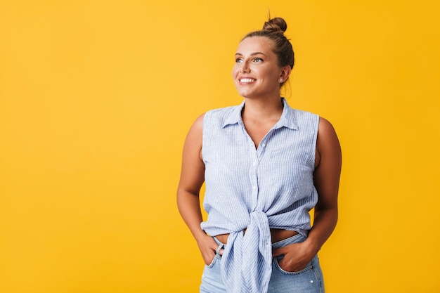 Linda garota sorridente de camisa e jeans alegremente olhando de lado sobre fundo amarelo isolado