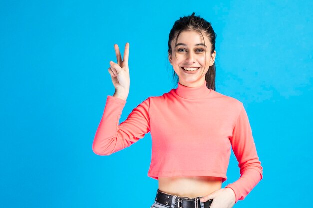 Linda garota sorridente em pé sobre fundo azul e gesto de paz