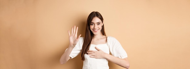 Foto grátis linda garota sorridente faz promessa coloca a mão no coração e diz a verdade sendo honesta jurando para você em pé