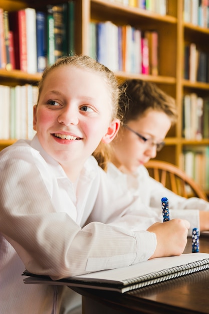 Foto grátis linda garota sorridente na mesa na biblioteca