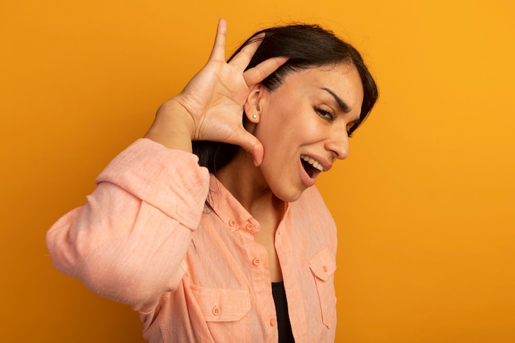 Foto grátis linda garota sorridente usando uma camiseta rosa mostrando um gesto de escuta isolado em amarelo
