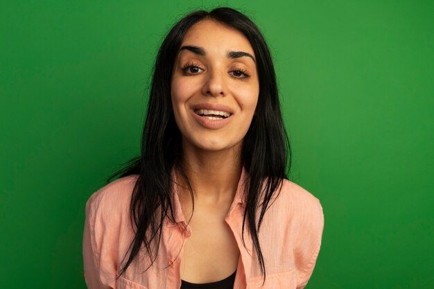 Linda garota sorridente, vestindo uma camiseta rosa isolada na parede verde