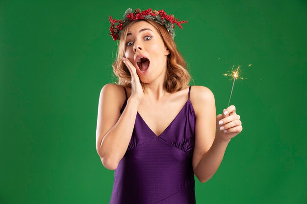 Linda garota surpresa com um vestido roxo com coroa, segurando estrelinhas, colocando a mão na bochecha isolada sobre um fundo verde com espaço de cópia