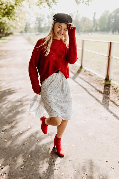 Linda garota usando sapatos vermelhos da moda e vestido branco na floresta Loira encantadora se sentindo feliz sob o sol na rua