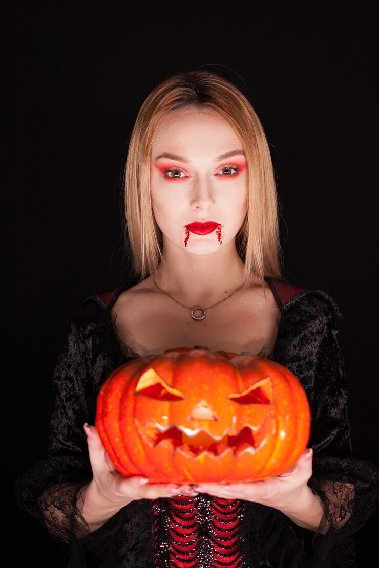 Foto grátis linda garota vestida como um vampiro segurando uma abóbora para o halloween sobre fundo preto.