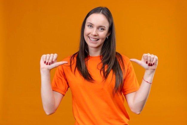 Foto grátis linda garota vestindo uma camiseta laranja apontando para si mesma, satisfeita e orgulhosa, sorrindo em pé sobre um fundo laranja isolado