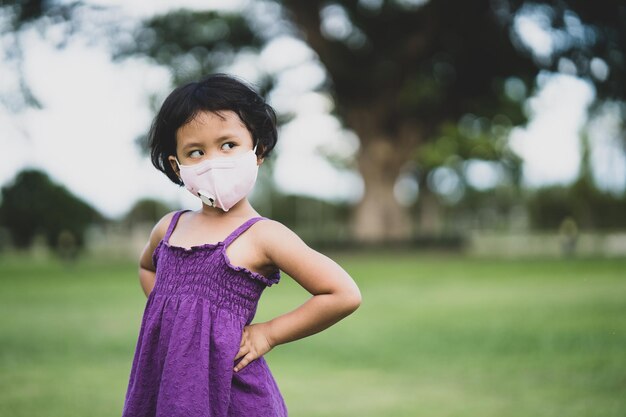 Linda garotinha asiática em uma máscara facial em pé ao ar livre