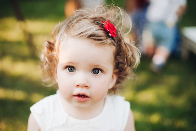 Linda garotinha caucasiana com cabelo curto ondulado loiro em um vestido branco no jardim