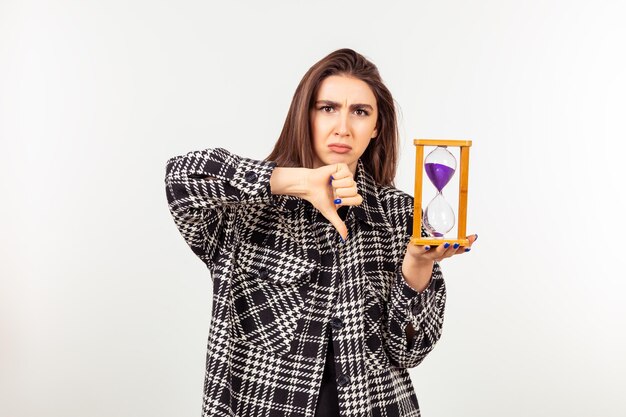 Linda jovem adora segurar a ampulheta e gesticular o polegar para baixo