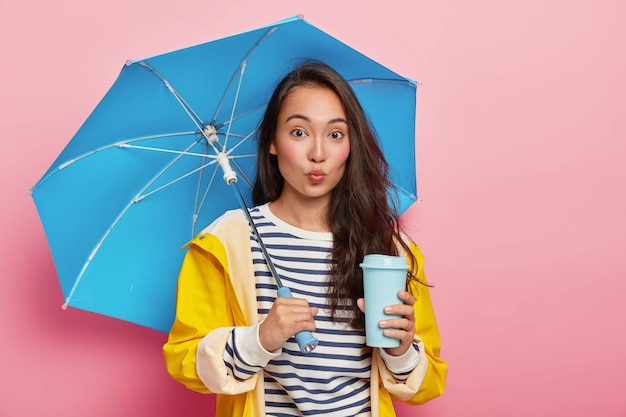 Linda jovem aluna asiática, a caminho da universidade durante um dia chuvoso, protege-se da umidade com guarda-chuva e capa de chuva