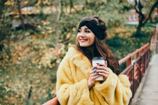 linda jovem bebe café em um copo na rua, ri e sorri