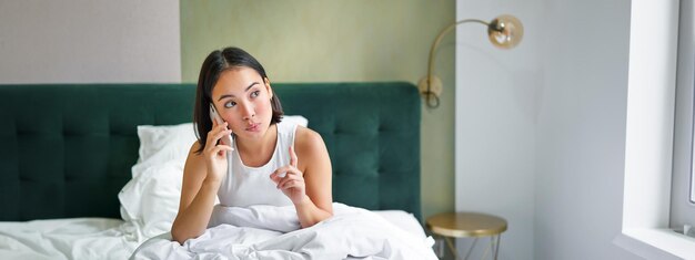 Foto grátis linda jovem coreana ligando para um telefonema na cama conversando com um amigo enquanto estava em casa