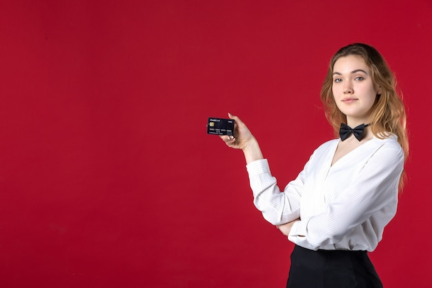 Linda jovem determinada mulher servidor borboleta no pescoço e segurando o cartão do banco sobre fundo vermelho