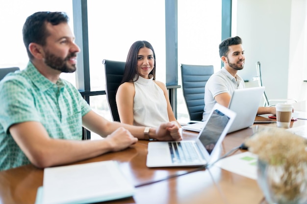 Linda jovem empresária fazendo contato visual enquanto está sentado entre colegas na mesa durante a reunião no escritório