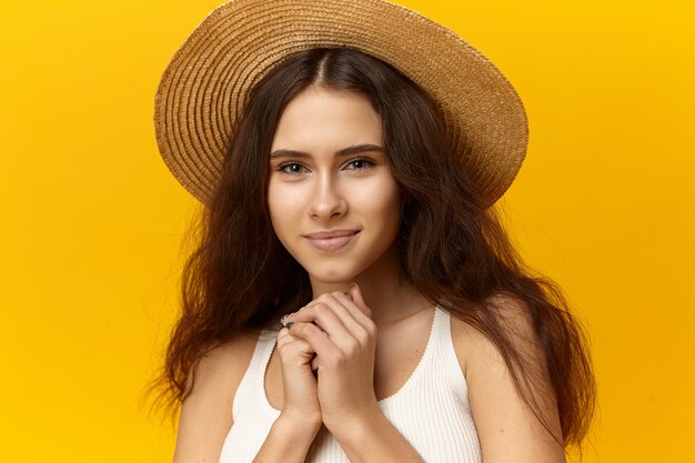 Linda jovem encantadora com pele bronzeada, maquiagem natural e cabelo solto posando em estúdio