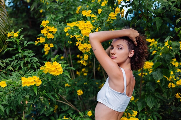 Linda jovem magro elegante em forma de mulher caucasiana feliz com blusa branca e calça jeans no parque cercado por flores amarelas tailandesas