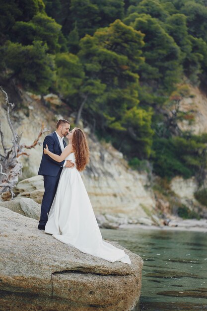 linda jovem noiva cabelos compridos em vestido branco com seu jovem marido perto do rio