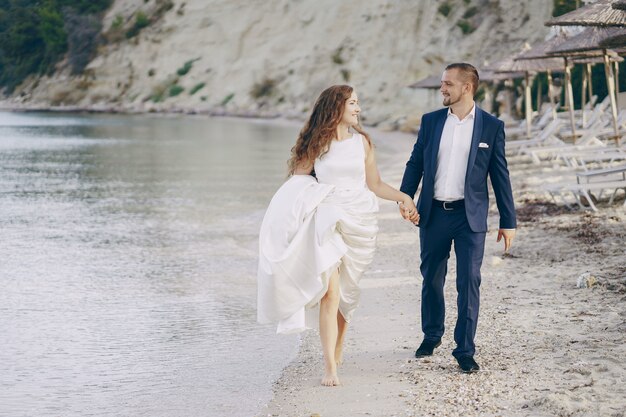 linda jovem noiva cabelos longos em vestido branco com seu jovem marido na praia