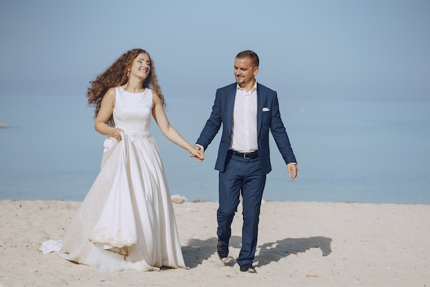 linda jovem noiva cabelos longos em vestido branco com seu jovem marido na praia