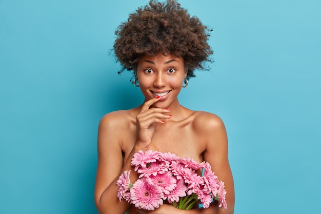 Linda jovem nua com penteado afro segurando lindo buquê de gérberas, pele saudável e bem cuidada, poses