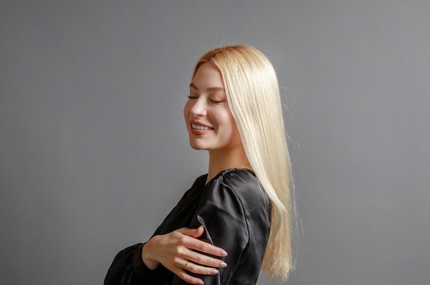 Linda jovem sorridente com a pele perfeita tocando o rosto com o conceito de beleza natural das mãos isolado no fundo cinza do estúdio