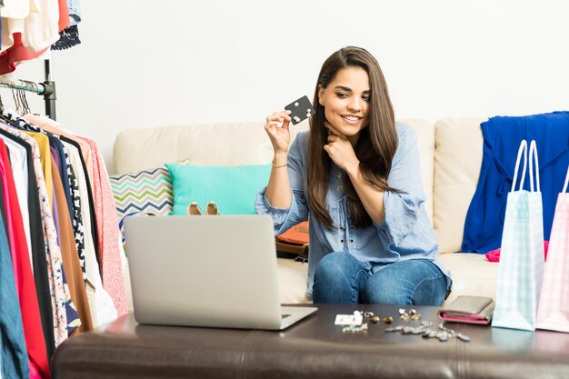 Linda jovem transmitindo um blog de moda ao vivo usando seu laptop em casa