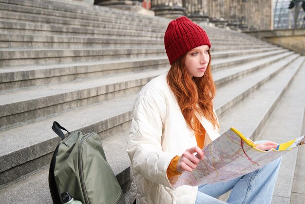 Foto grátis linda jovem viajante com mochila segura mapa de papel explora planos turísticos da cidade rota f