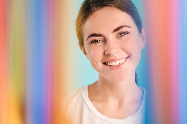 Foto grátis linda linda garota olhando alegremente na câmera através do arco-íris sobre fundo colorido isolado