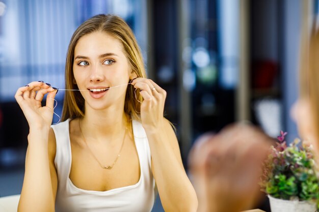 Linda loira jovem usa fio dental para cuidar dos dentes.