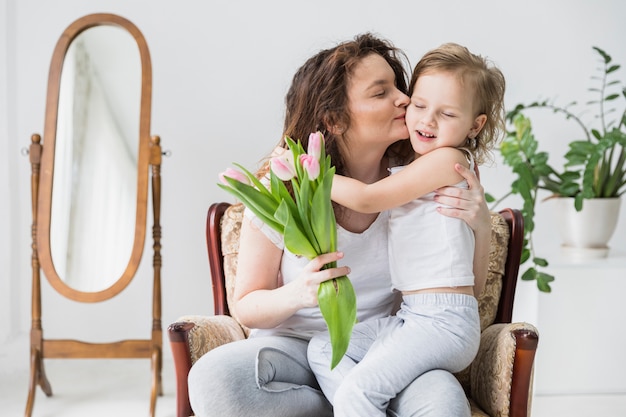 Linda mãe beijando seu filho em casa segurando o monte de flores de tulipa