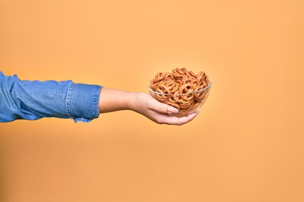 Foto grátis linda mão de mulher segurando a tigela com pretzels alemães cozidos sobre fundo amarelo isolado