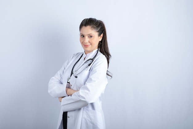 Foto grátis linda médica nos braços eretos de jaleco branco cruzados sobre uma parede branca.